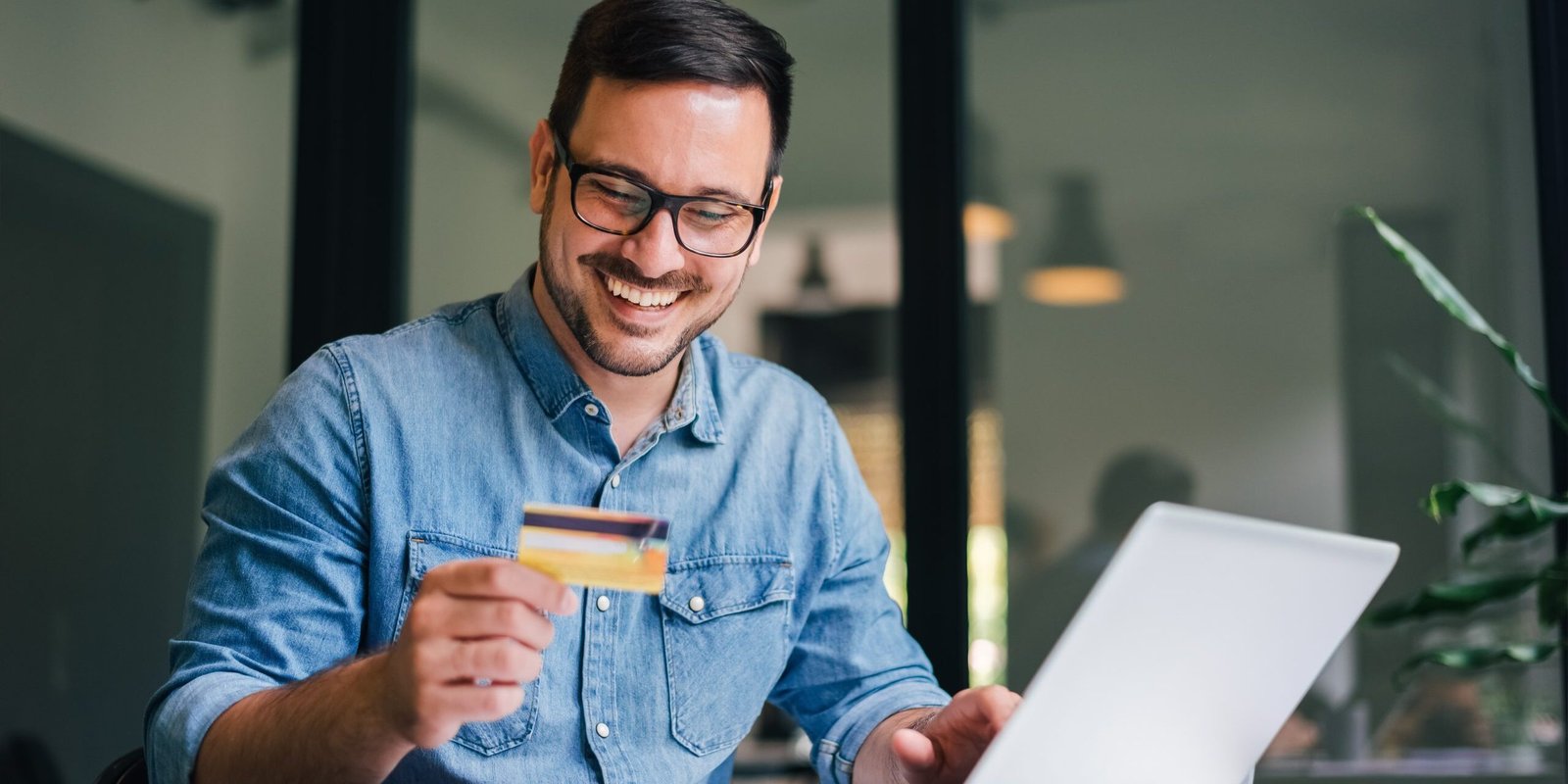 Happy cheerful smiling young adult man doing online shopping or e-shopping satisfied entrepreneur making online payment paying for service or goods self employed freelancer collecting fee